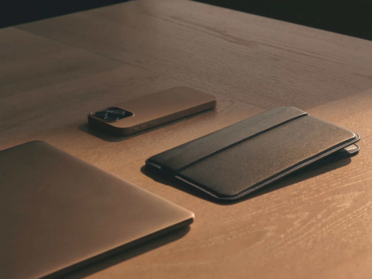 Skrivebord i blødt vinduslys med telefon, tablet og laptop-sleeve